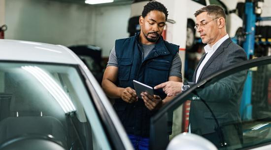 Two men in a service garage, standing next to open car door looking at a mobile tablet