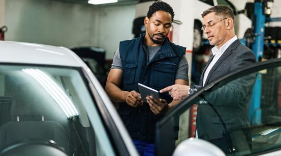 Two men in a service garage, standing next to open car door looking at a mobile tablet