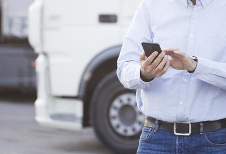 Man looking at mobile phone standing in front of semi trucks